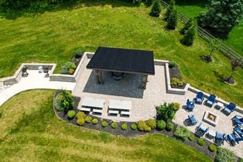 A patio with a fire pit and chairs is surrounded by a grassy area.